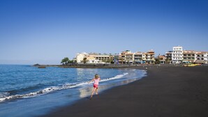A beach with a child running along the shore, buildings in the background, and clear blue skies. - Hotel Playa Calera (Valle Gran Rey)