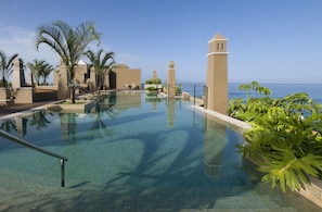 A clear pool with a view of the ocean, palm trees, and a building with a tower. - Hotel Playa Calera (Valle Gran Rey)