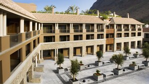 A multi-story hotel with a courtyard featuring planters with trees and benches. - Hotel Playa Calera (Valle Gran Rey)