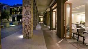 A hotel corridor with stone pillars, a dining area with tables set for guests, and a view of the building's exterior at dusk. - Hotel Playa Calera (Valle Gran Rey)