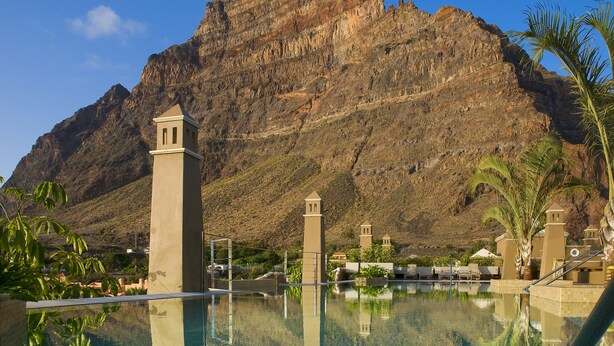 A clear pool with a mountain backdrop, a tower structure, and palm trees. - Hotel Playa Calera (Valle Gran Rey)