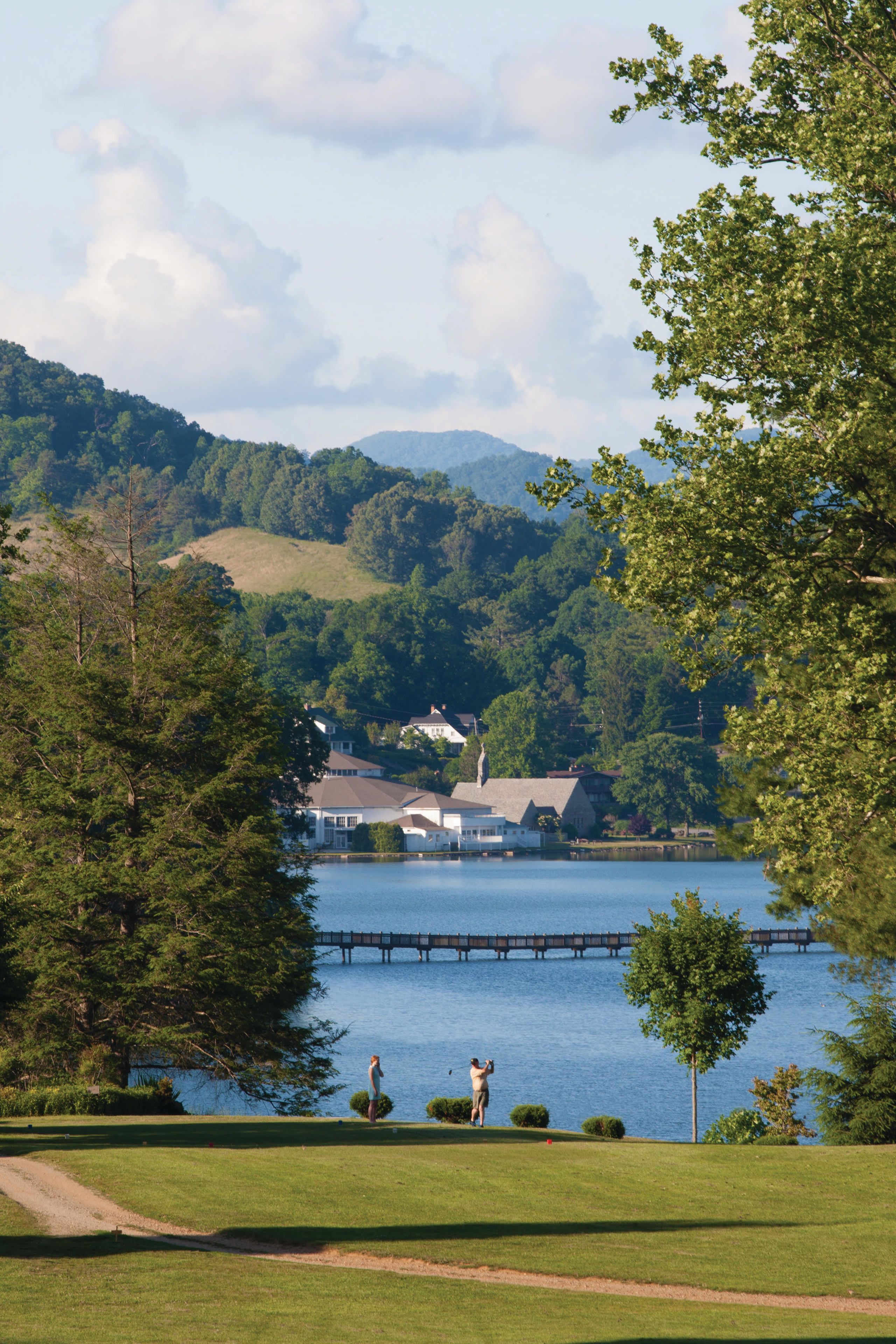 A lakeside view with a bridge, houses, and a golf course.