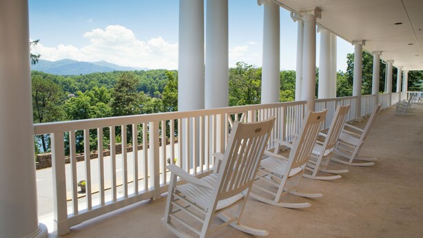 A covered porch with white columns and a railing, overlooking a lush green landscape with mountains in the distance. - Lambuth Inn at Lake Junaluska (Lake Junaluska)