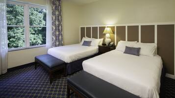 Una habitación de hotel con dos camas, un banco, una mesita de noche con lámpara y una ventana con cortinas.