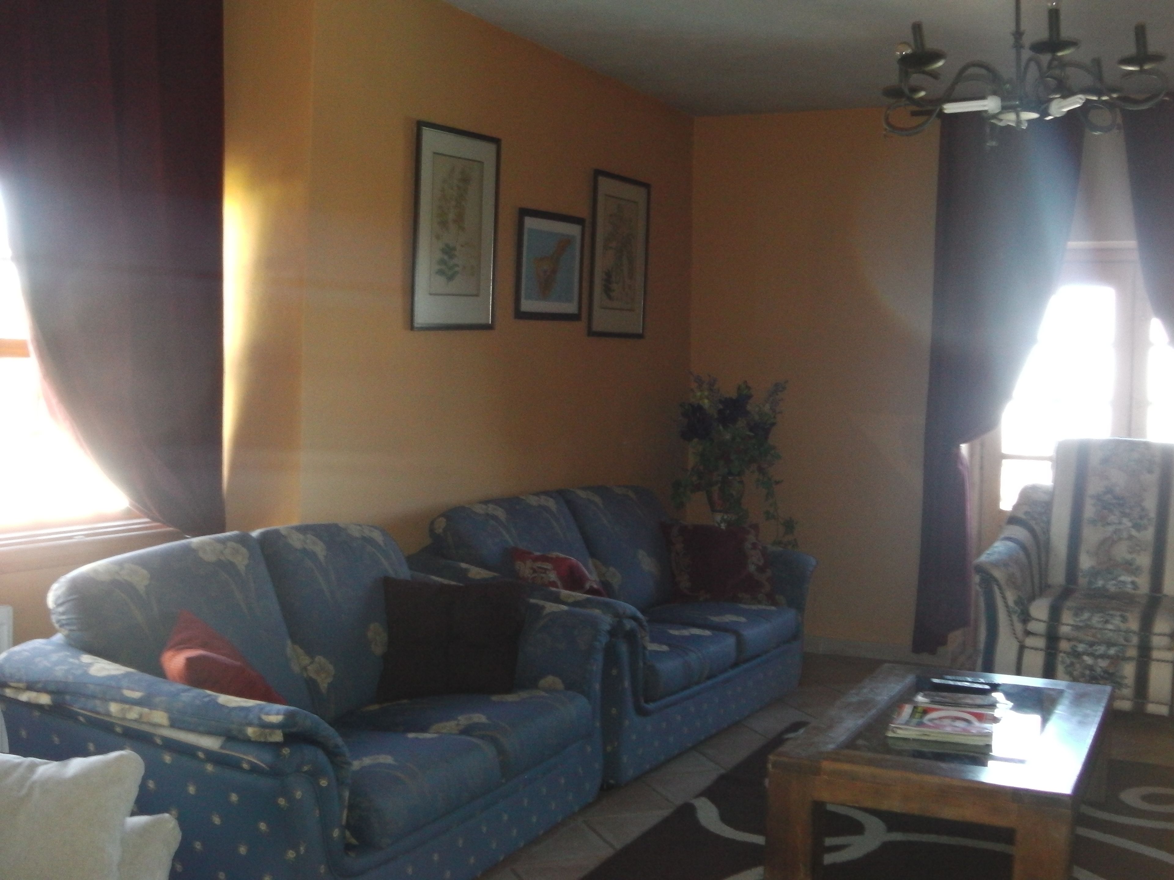 A living room with a blue sofa, a wooden coffee table, and a chair. There are two framed pictures on the wall.