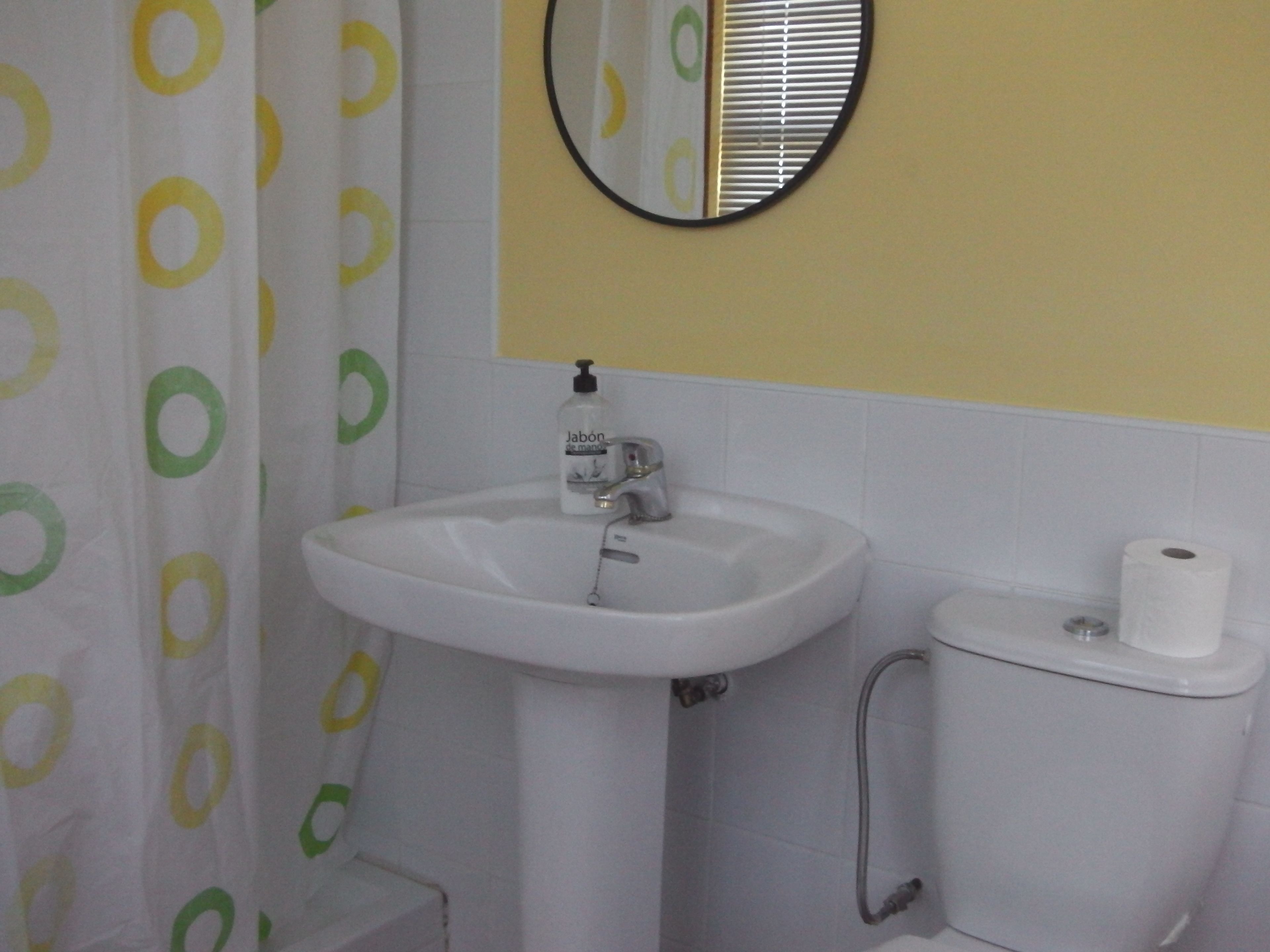 A bathroom with a white sink, toilet, and shower curtain with green and yellow circles.
