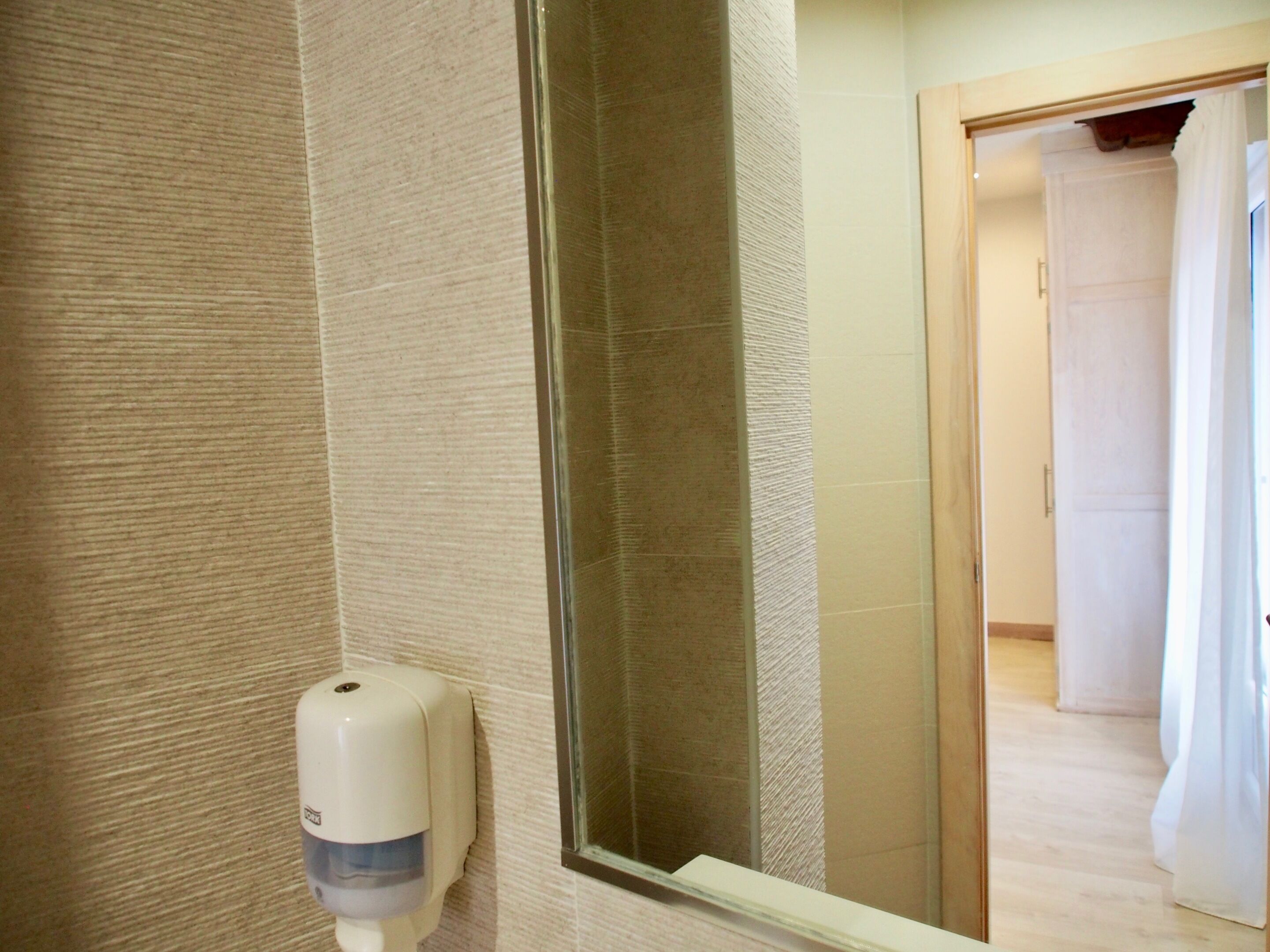 Un bagno con un dispenser di gel igienizzante, uno specchio e una zona doccia.