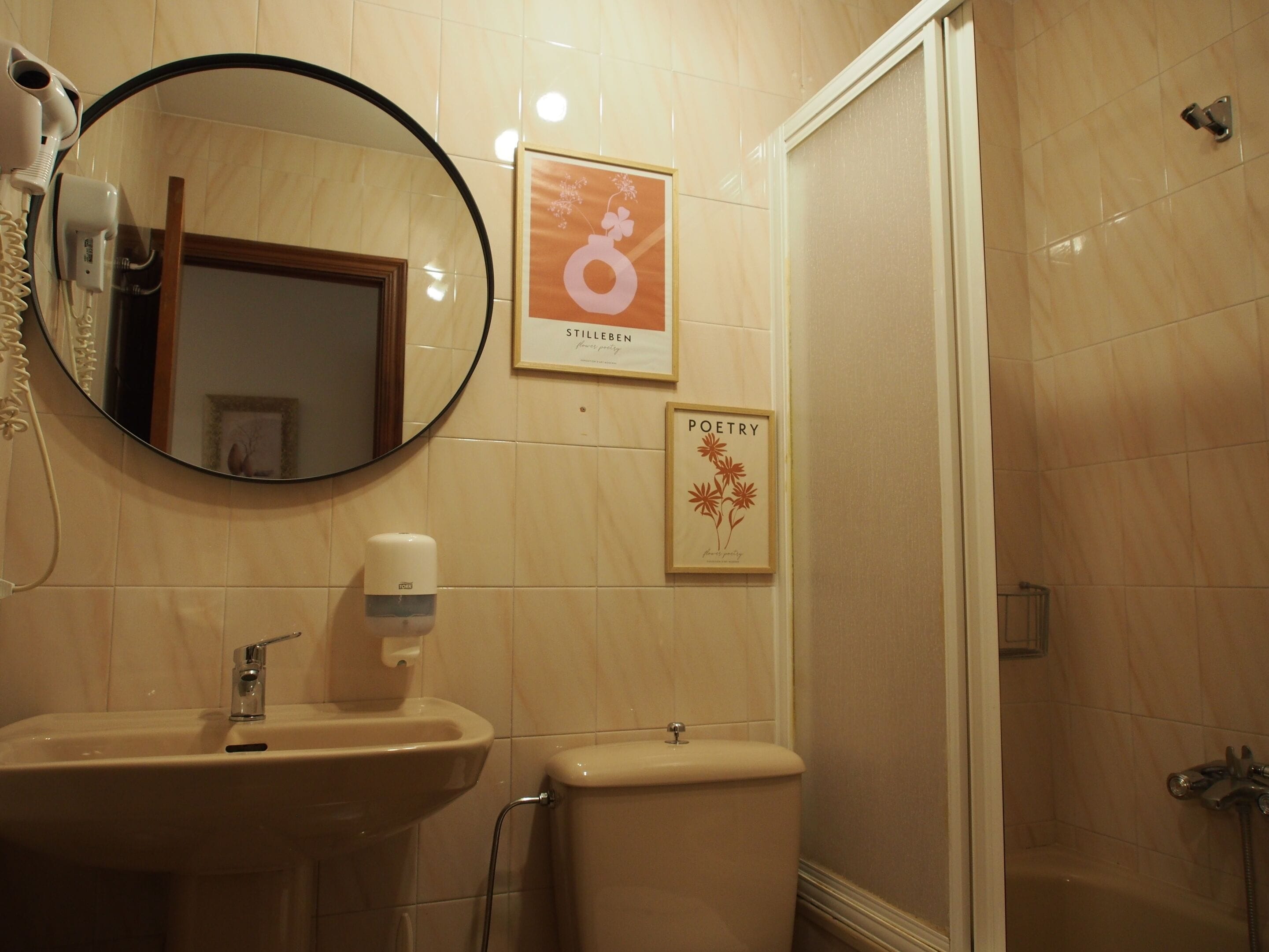 A bathroom with a sink, toilet, and a shower. There are framed pictures on the wall.