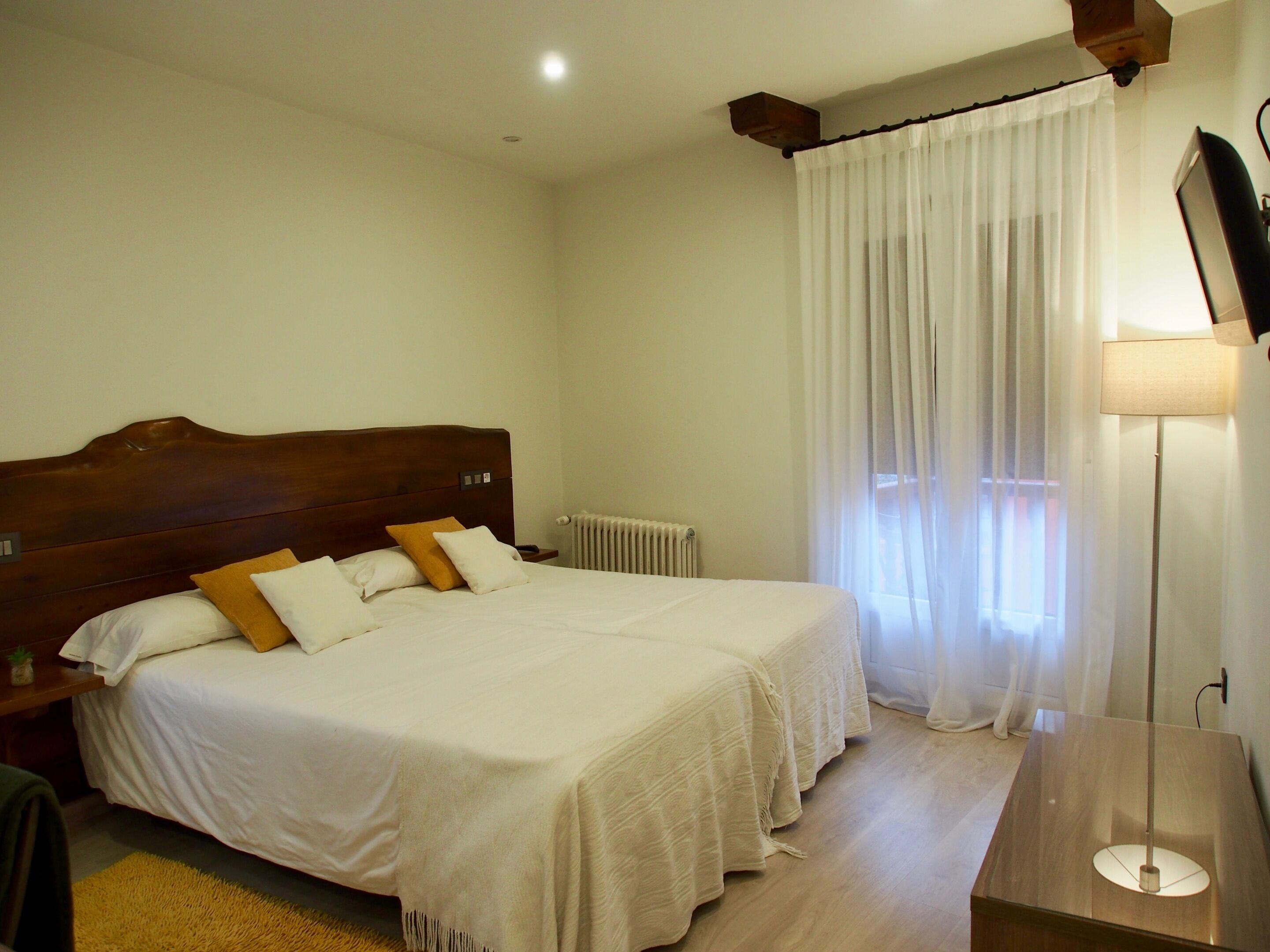 Un lit double avec une tête de lit en bois, deux tables de chevet, une lampe sur pied et un radiateur.
