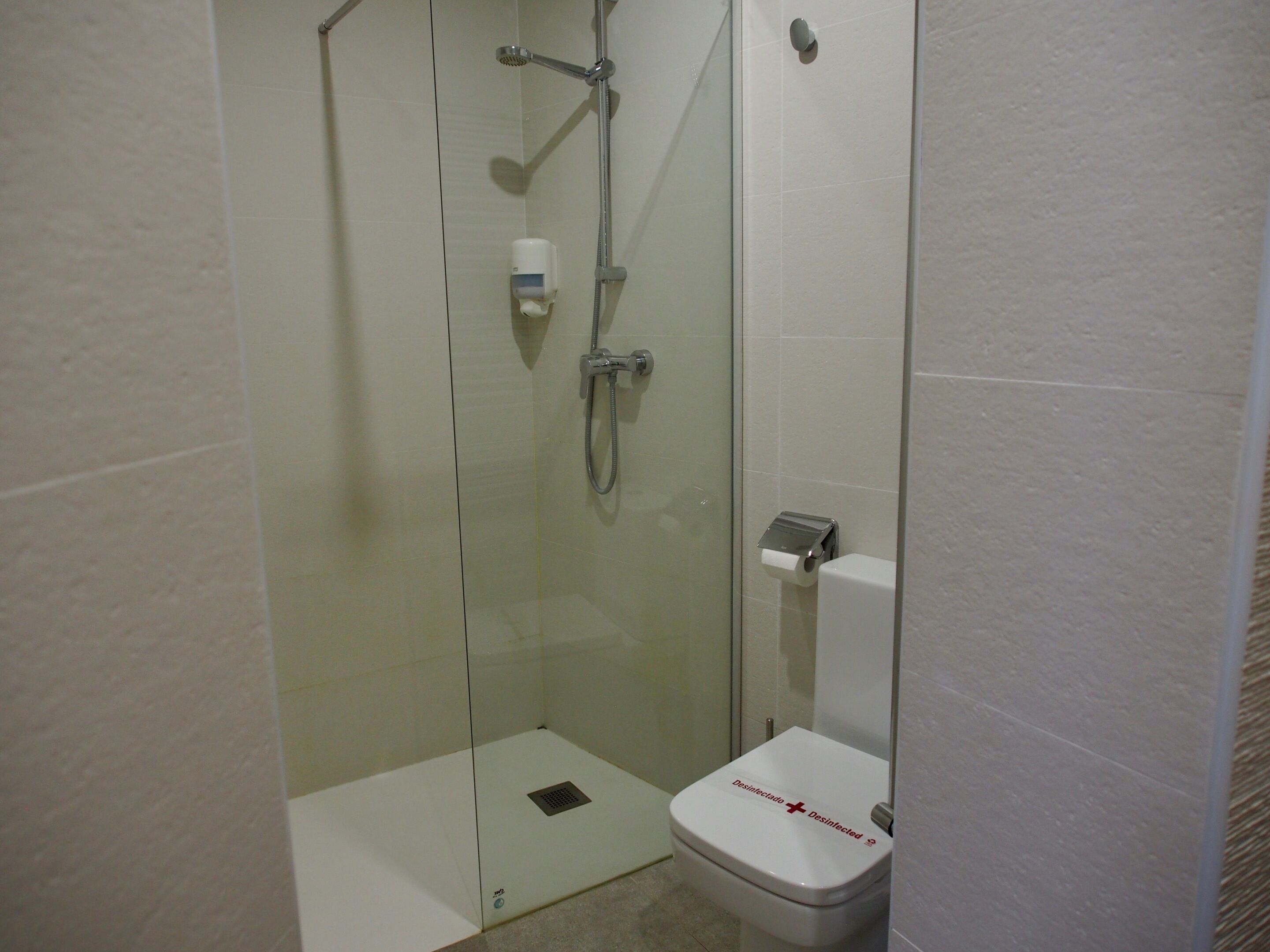 A small, modern bathroom with a glass-enclosed shower, a toilet, and a hand dryer.