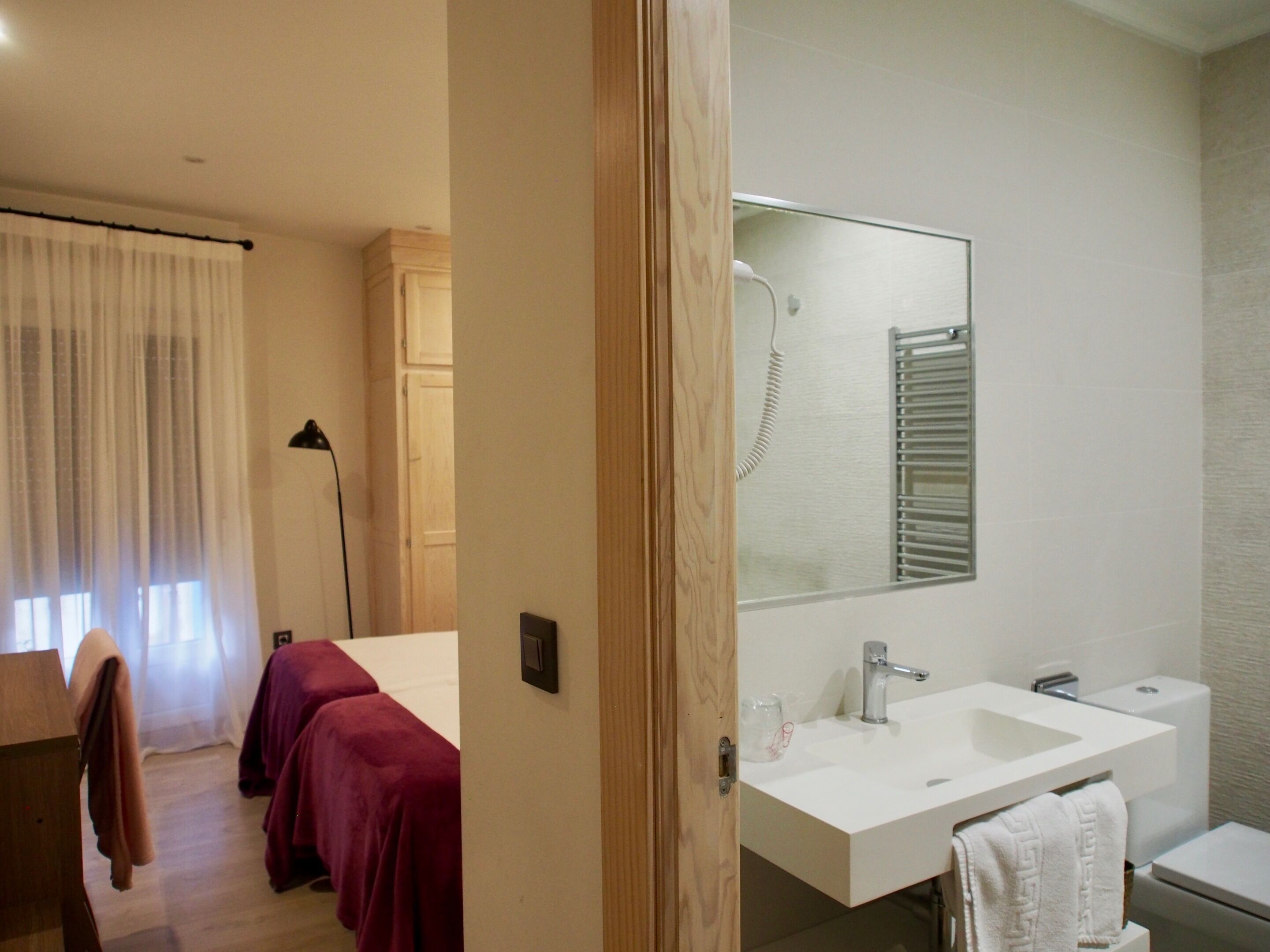 A hotel room with a large bed, a bedside table, a mirror, a white sink, and a toilet.