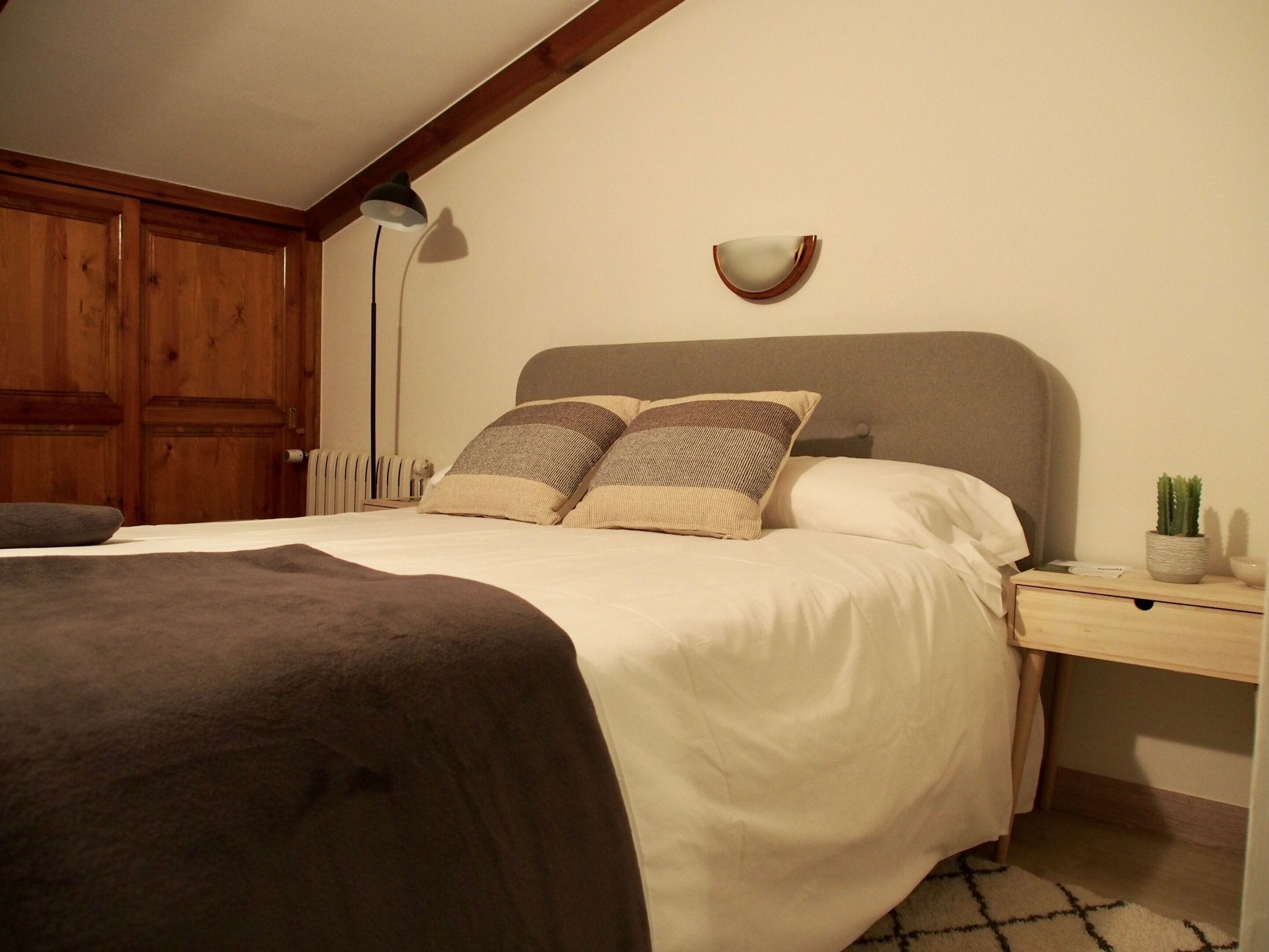 Een slaapkamer met een bed, nachtkastje, lamp en een kleine plant in pot.