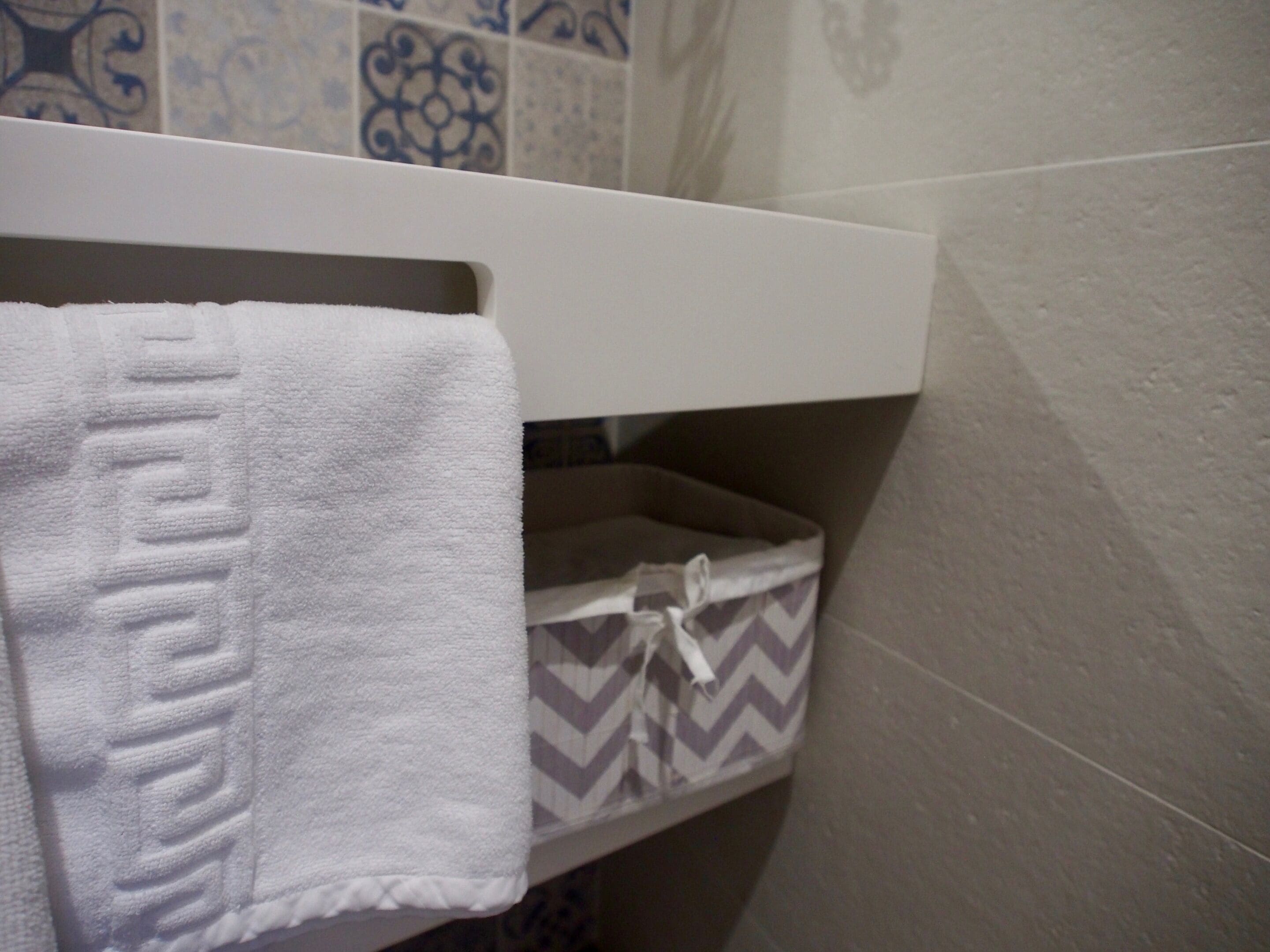 A bathroom with a towel hanging on a rack, a patterned storage box, and a tiled wall.