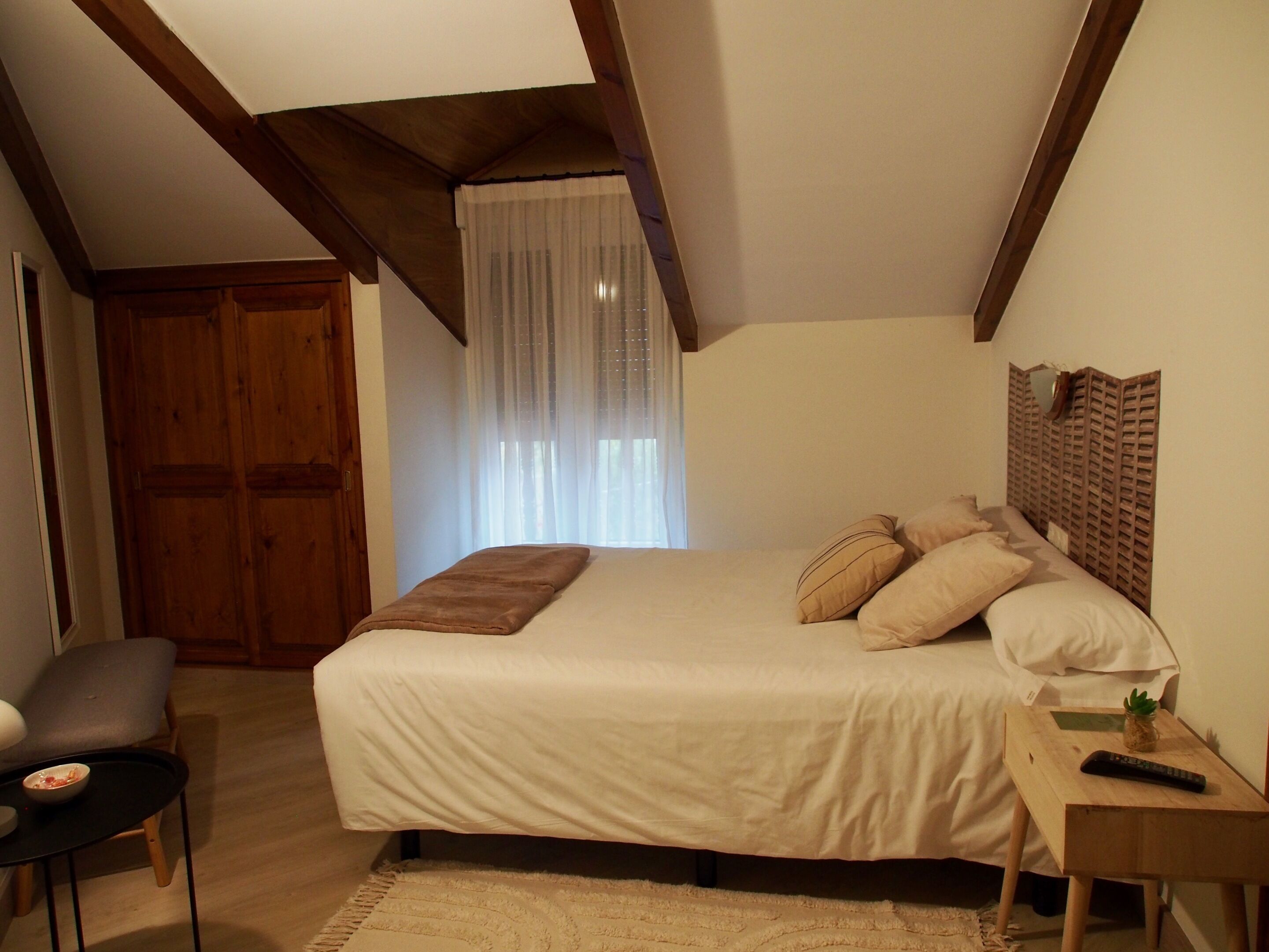 A bedroom with a bed, a nightstand, a chair, and a wooden wardrobe.