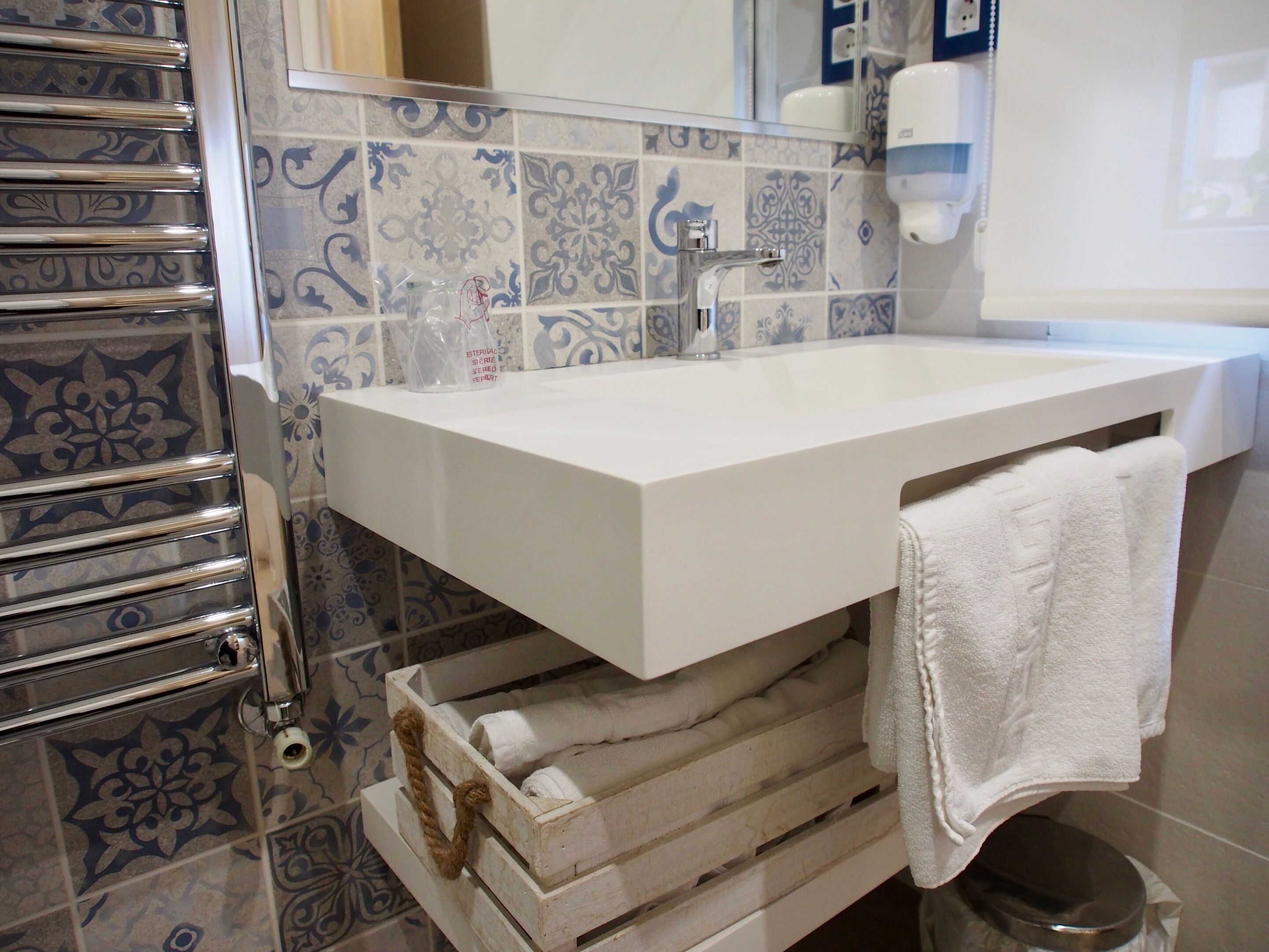 Un baño con un lavamanos blanco, un perchero y baldosas estampadas.