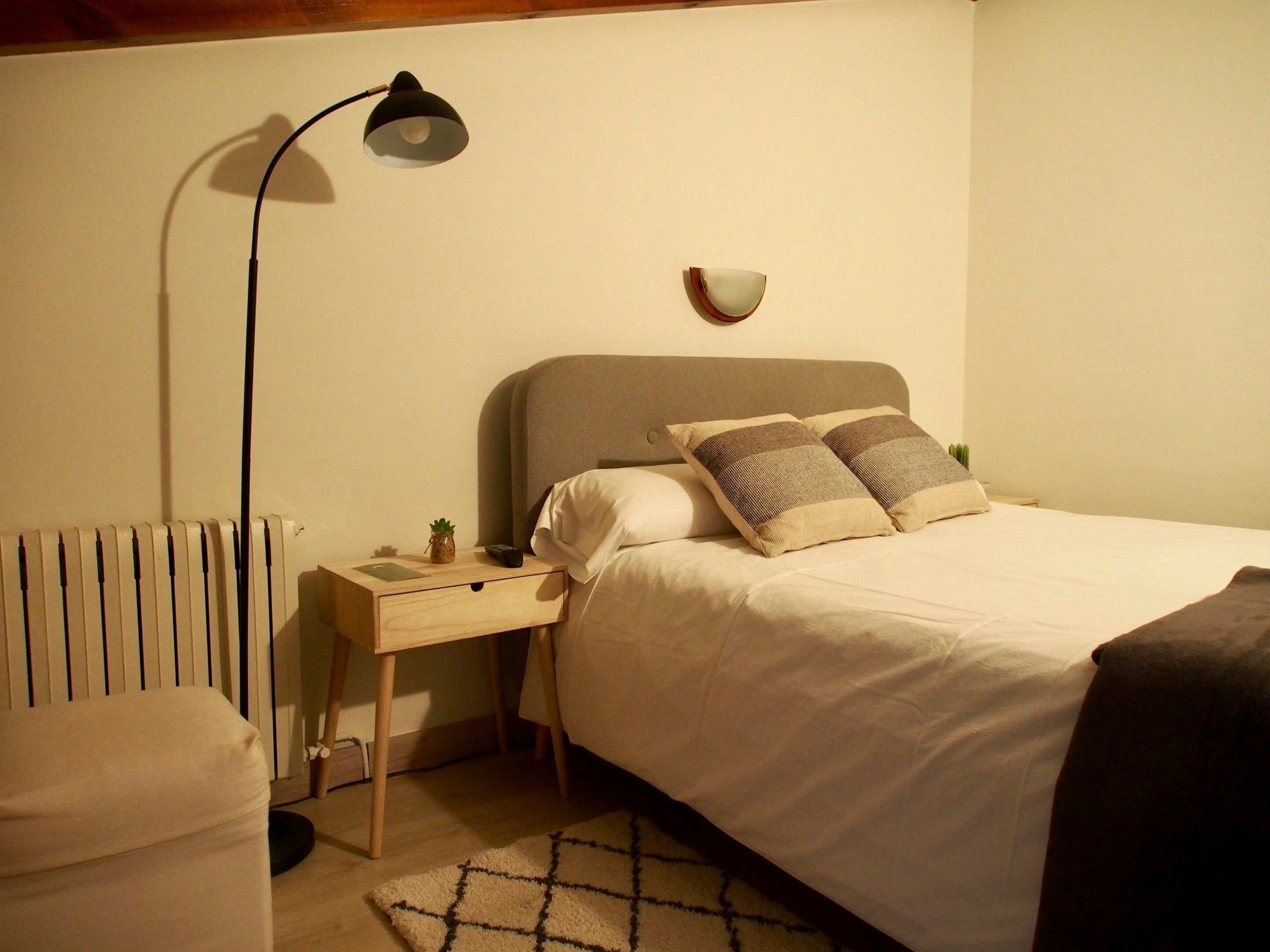 Una camera da letto ordinata con un letto, un comodino, una lampada e una piccola pianta.