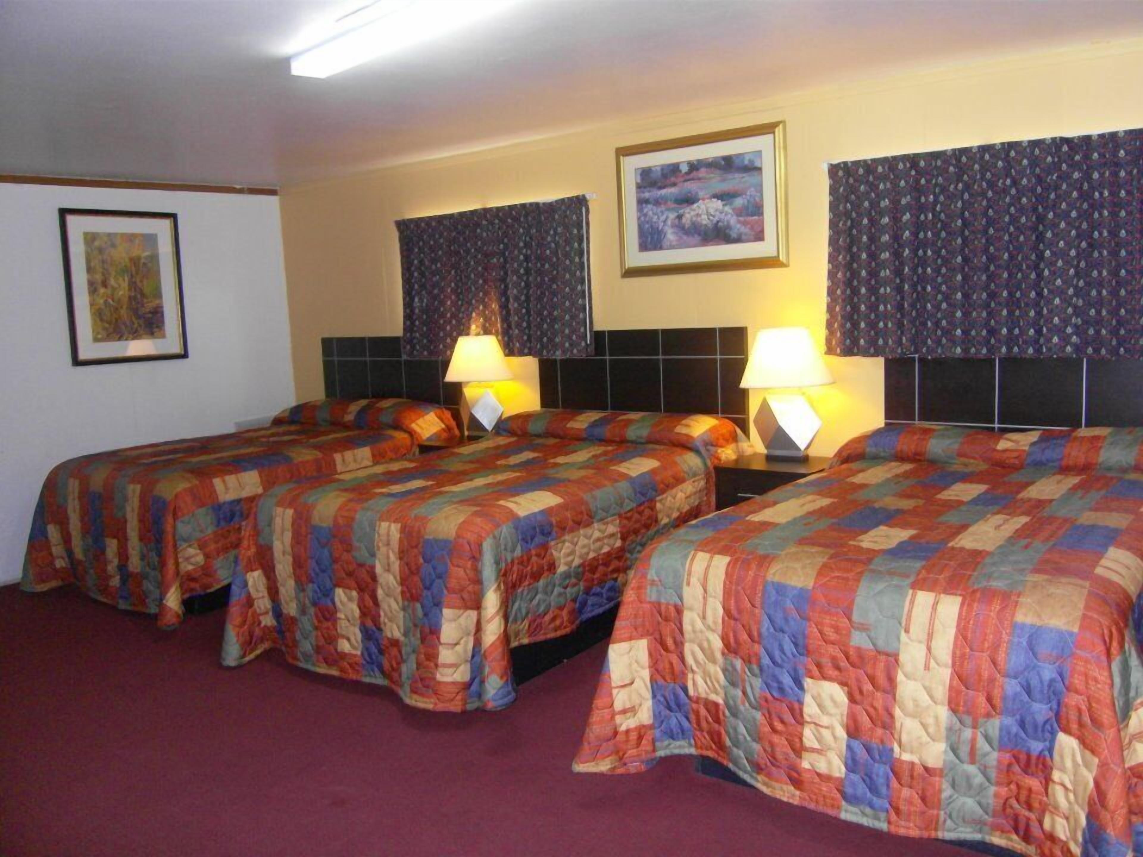 Une chambre d’hôtel avec deux lits, chacun agrémenté d’une couverture colorée, d’une tête de lit et d’une table de chevet avec une lampe.