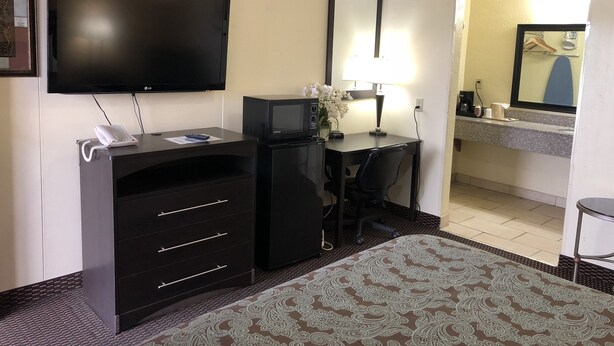Hotelkamer met een flatscreen televisie, bureau met lamp, spiegel, telefoon en een kamerbreed tapijt met patroon.