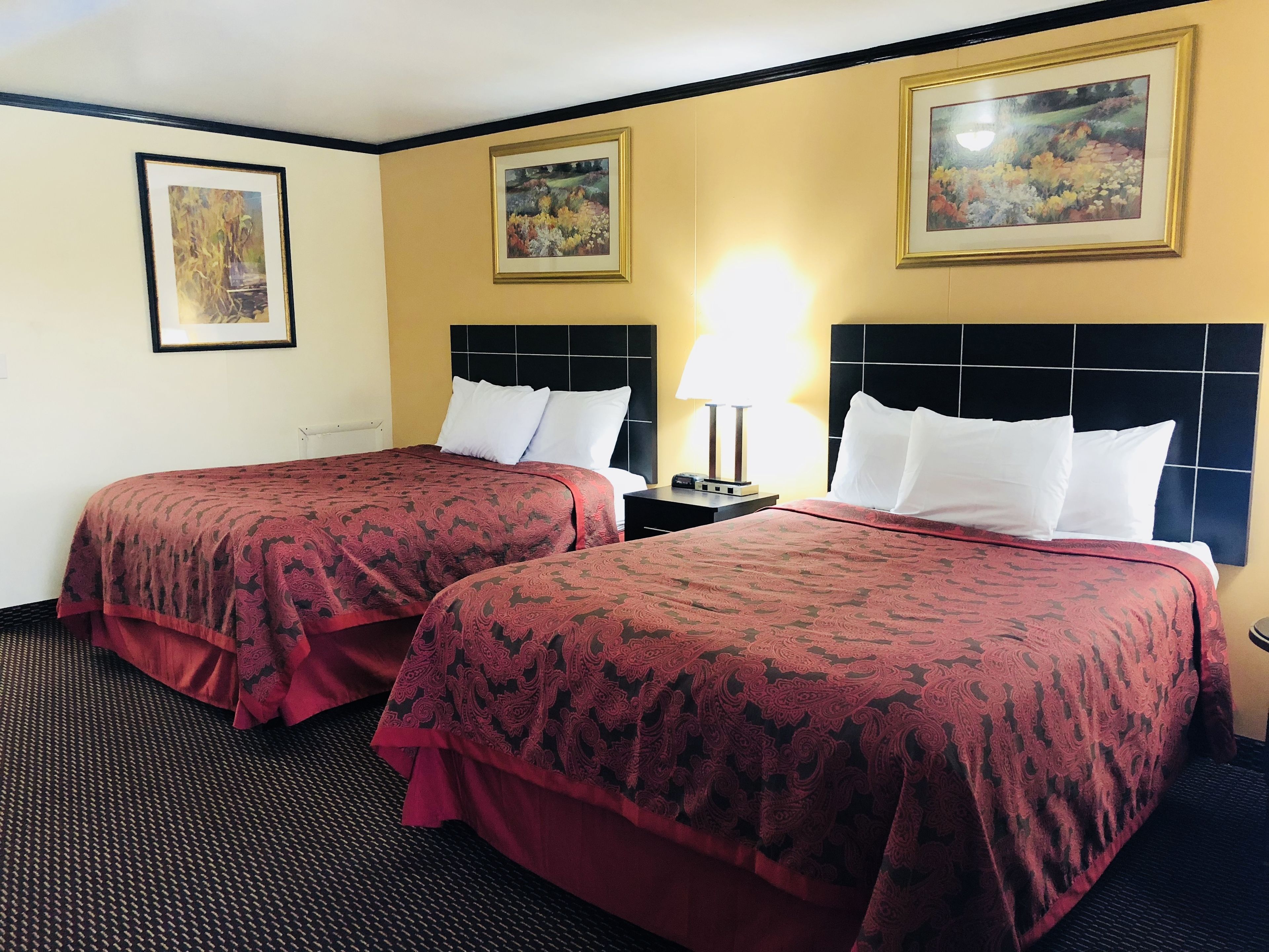 A hotel room with two beds, each with a patterned bedspread, a black headboard, and a nightstand with a lamp.