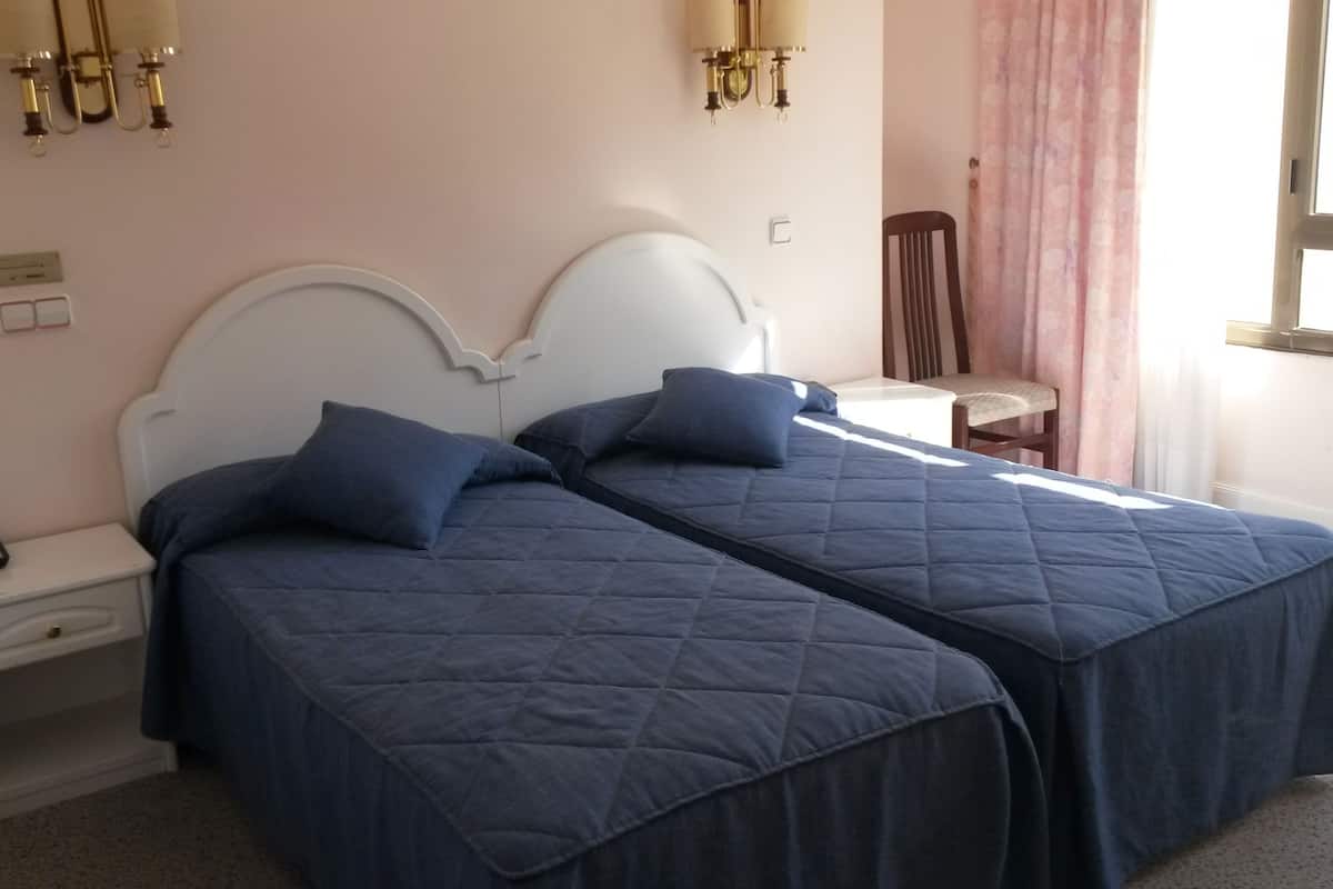 Habitació d'hotel amb dos llits, una taula de nit, una cadira i una finestra amb cortines.