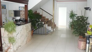 Zona de recepción con mostrador de mármol, una escalera y plantas en macetas.