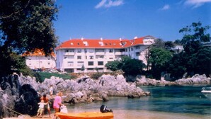 Un hotel costero con un edificio de techo rojo, costa rocosa y un pequeño bote en el agua.