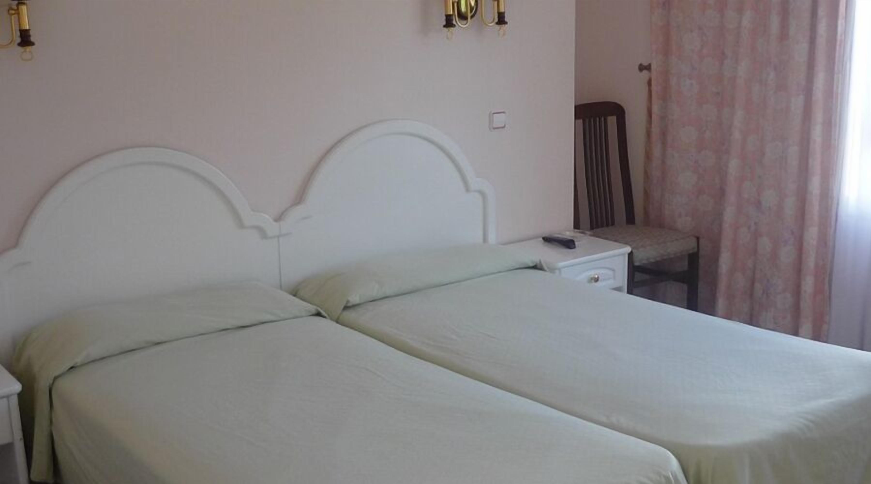 A double bed with a white headboard and a bedside table with a remote control.