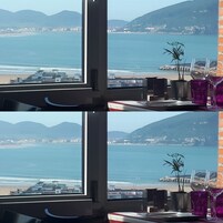 A room with a large window overlooking a beach and mountains. There are two potted plants and a tray with glasses on the windowsill.