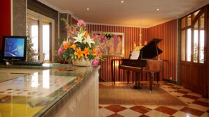 A hotel lobby with a piano, a large floral arrangement, a computer, and a checkered floor. - Hotel Risco (Laredo)