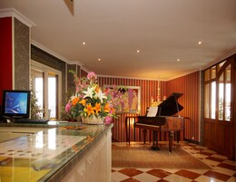 Vestíbulo de hotel con un piano, un arreglo floral grande, una computadora y un piso a cuadros.