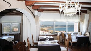 A dining area with tables set for two, wooden chairs, and a view of the sea through large windows. - Hotel Risco (Laredo)