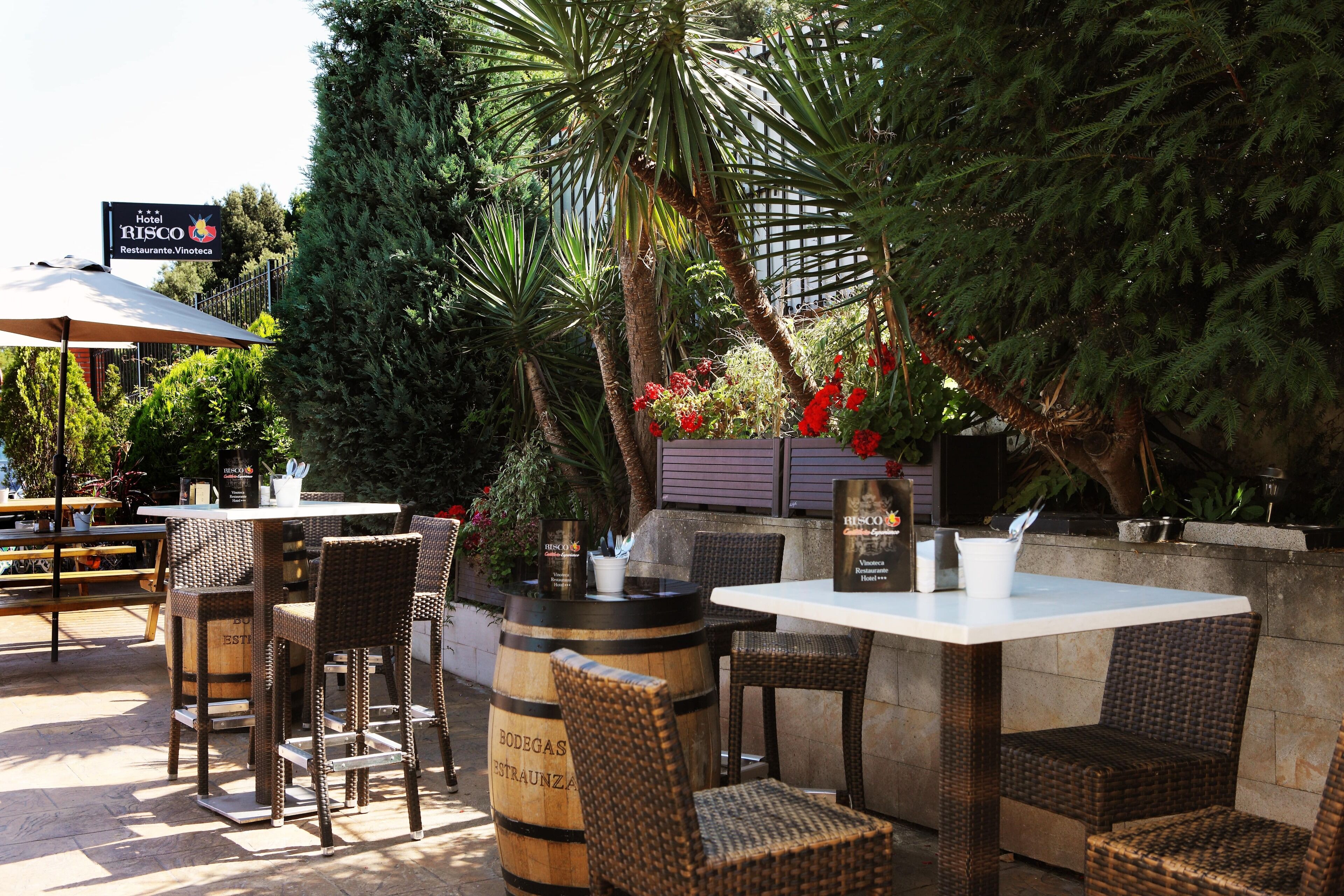 Un espace extérieur aménagé en terrasse, avec des meubles en osier, une table blanche et un tonneau portant l’inscription « BODEGAS RESTRANZA ».