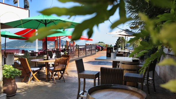 An outdoor patio with wicker furniture, wooden tables, and green umbrellas. - Hotel Risco (Laredo)