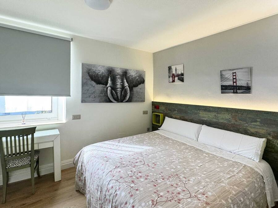 Une chambre à coucher avec un lit, un bureau et une chaise. Deux œuvres d’art sont accrochées au mur et représentent un éléphant et un pont.