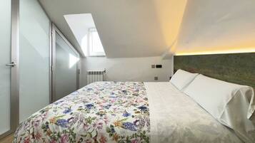 Quarto com claraboia, cama com colcha florida e cabeceira com acabamento texturizado.