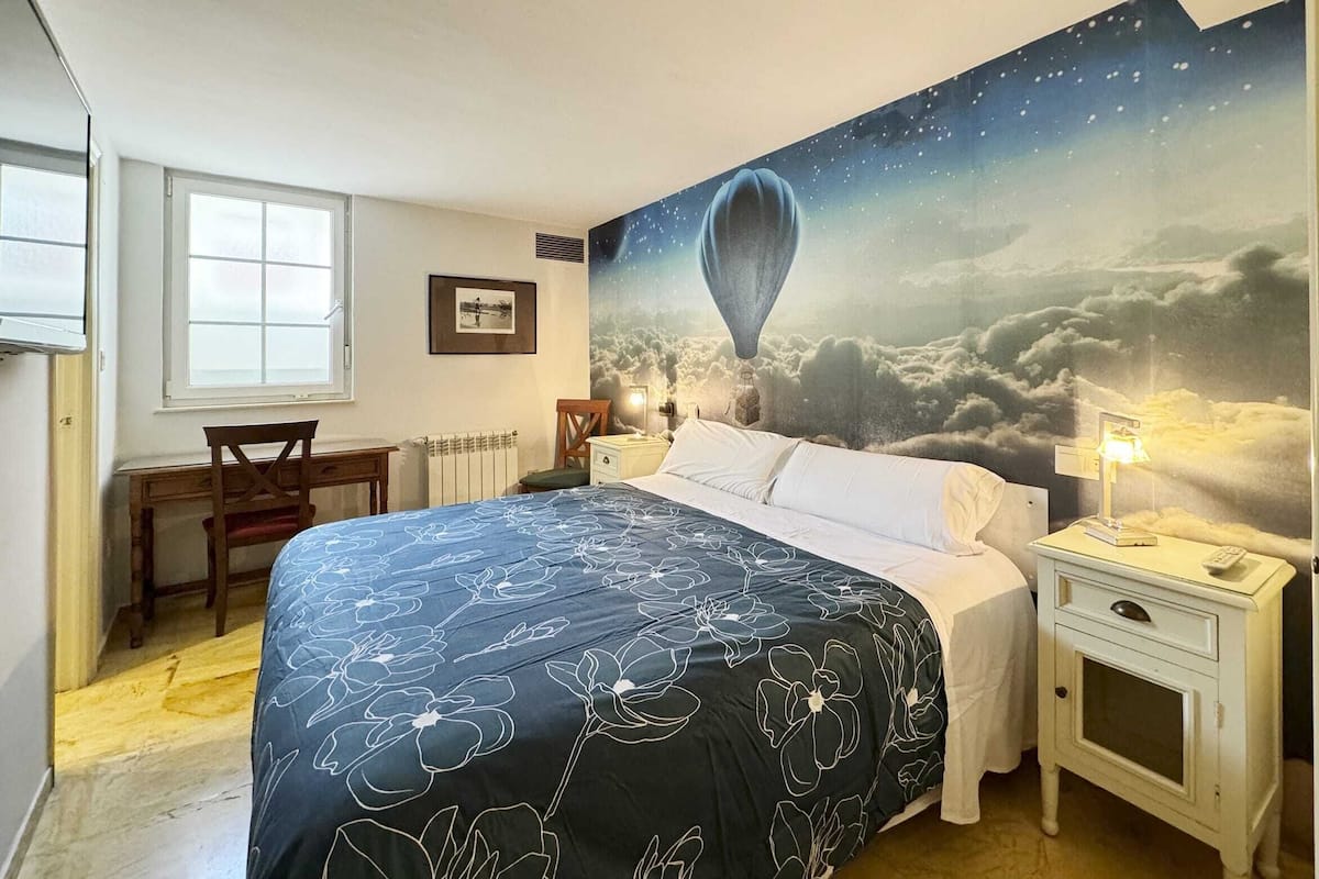 Ein Schlafzimmer mit einem großen Bett, einem Schreibtisch, einem Stuhl, einem Nachttisch und einem Wandgemälde mit einer Heißluftballon-Motivs.
