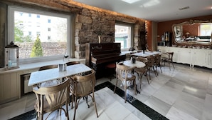 Une pièce spacieuse avec un mur en pierre, un piano, un coin repas avec des chaises et une table, et un coin cuisine avec des placards et un grand miroir.