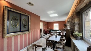 A dining area with a marble table and chairs, a large framed artwork on the wall, and a stone wall with a window.