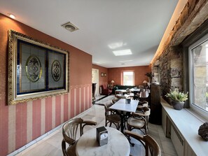 A dining area with a marble table and chairs, a large framed artwork on the wall, and a stone wall with a window.
