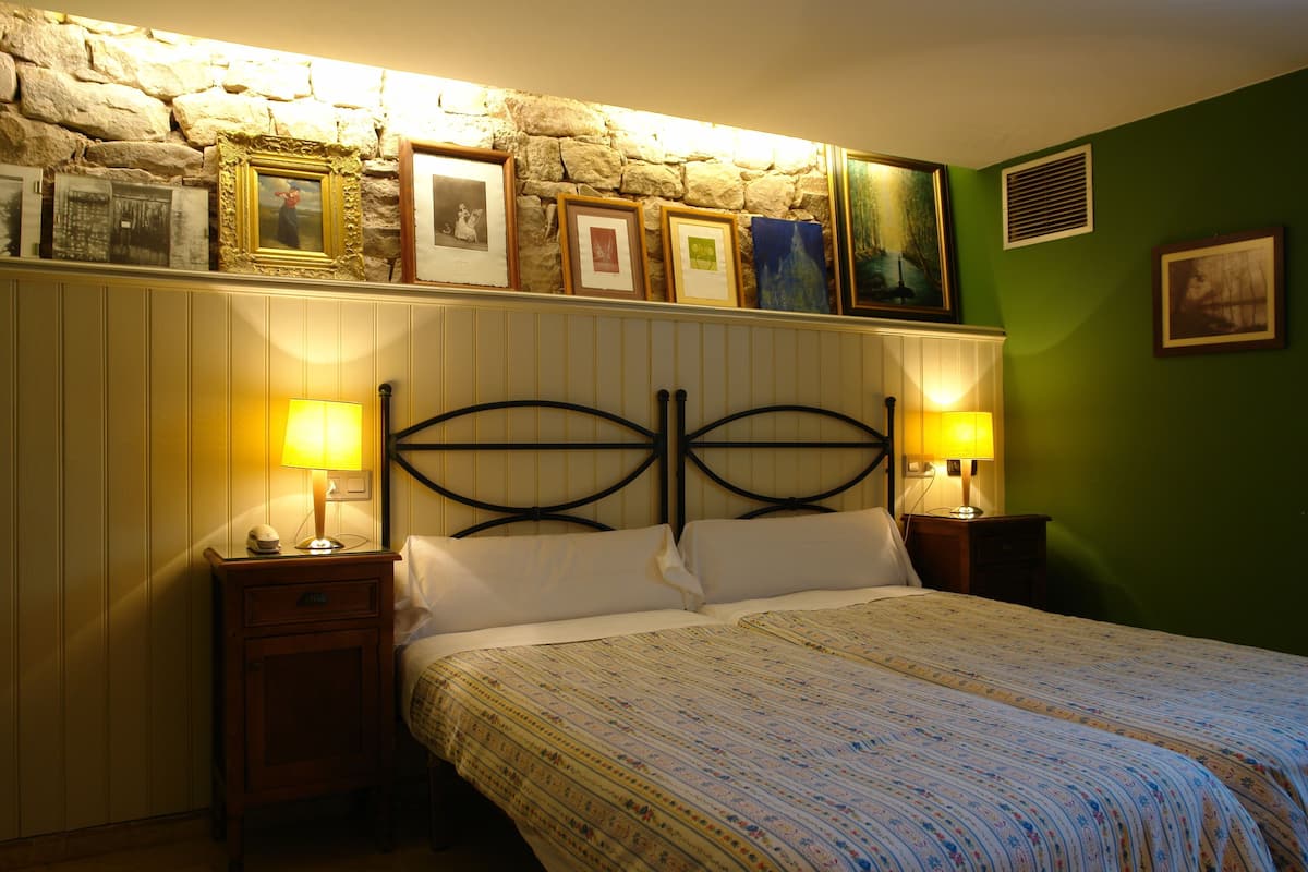 Ein Schlafzimmer mit Stehwänden, einem Bett mit weißen Bettbezügen, zwei Nachttischlampen und gerahmten Bildern über dem Bett.