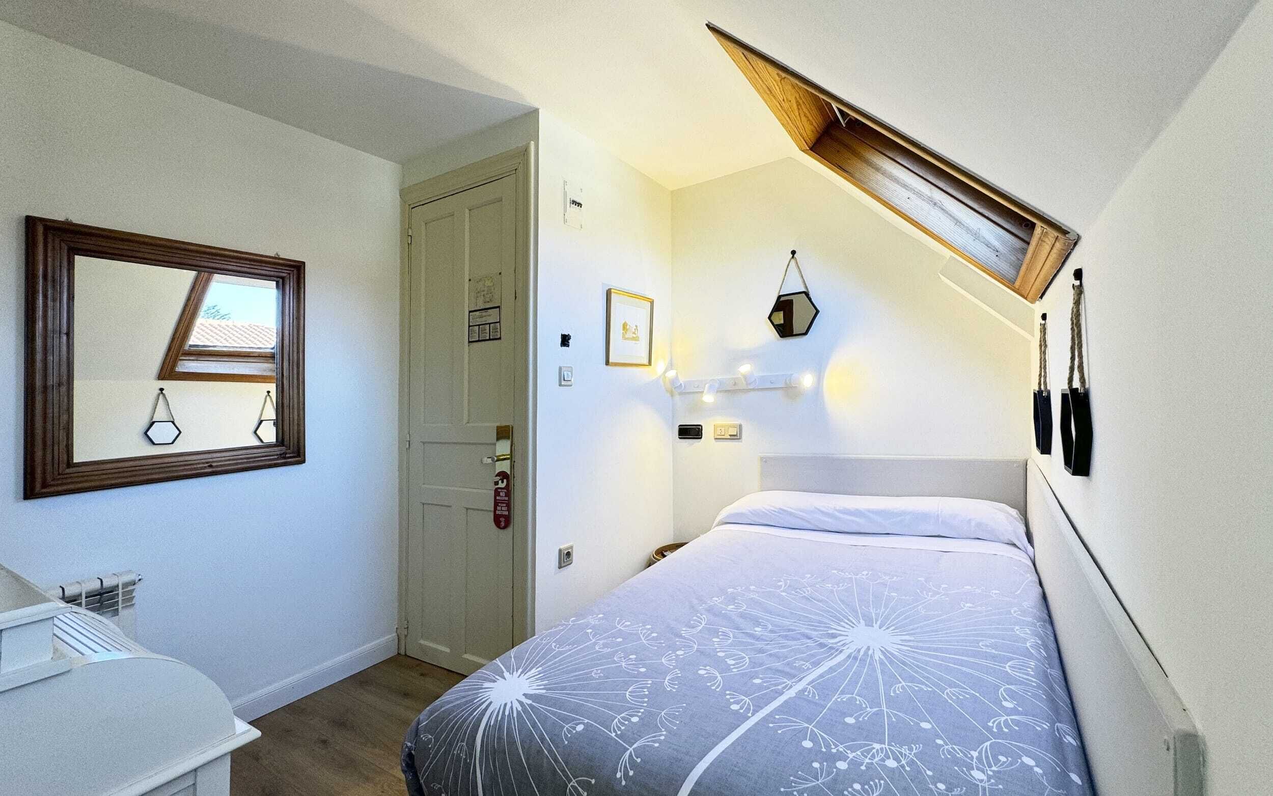 A bedroom with a bed, a mirror, a door, and a small window.