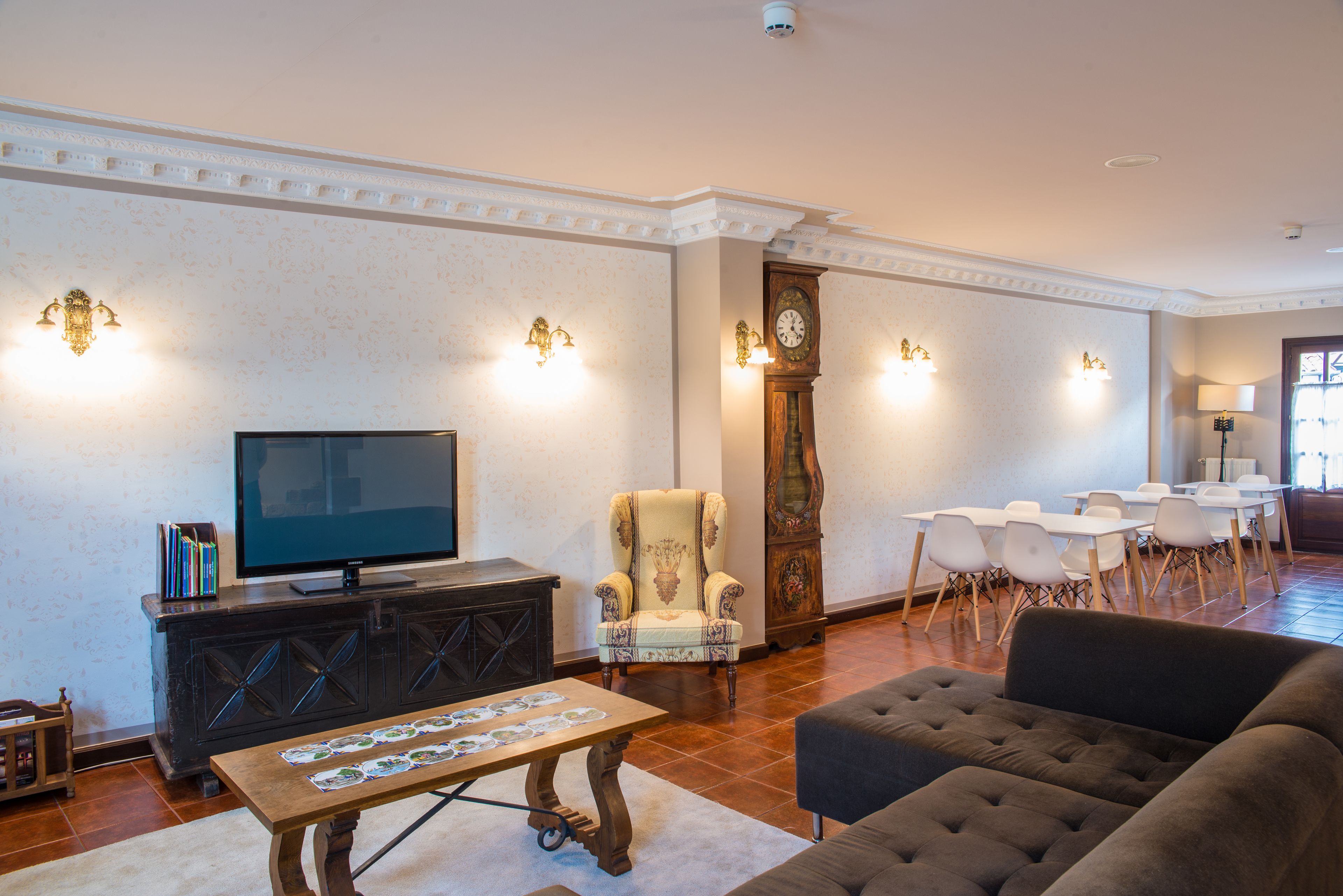 A spacious living room with a television, a large armchair, a sofa, and a dining area with chairs and tables.