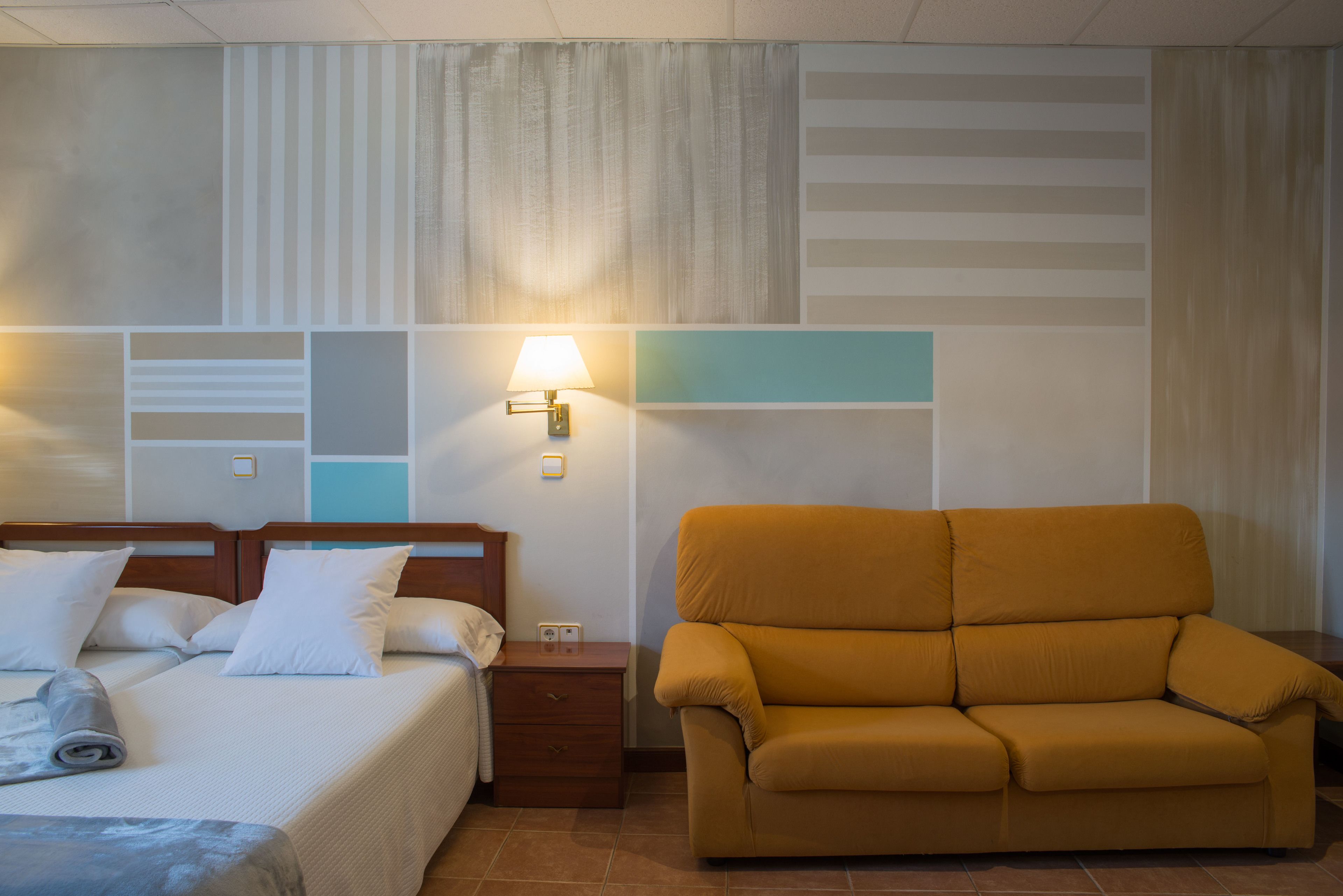 A hotel room with a bed, a nightstand, a lamp, and a sofa.