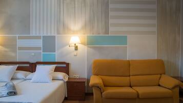 A hotel room with a bed, a nightstand, a lamp, and a sofa.