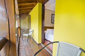 A room with a wooden floor, a bed with white linens, and a chair. - Apartamentos Capriccio (Santillana del Mar)