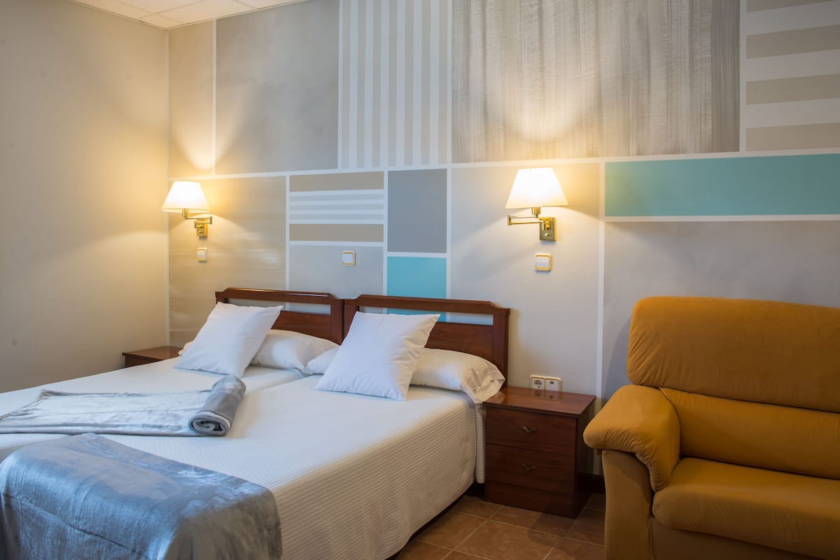 Une chambre d’hôtel avec un lit, deux tables de chevet, une lampe, une chaise et un mur orné d’un motif géométrique.