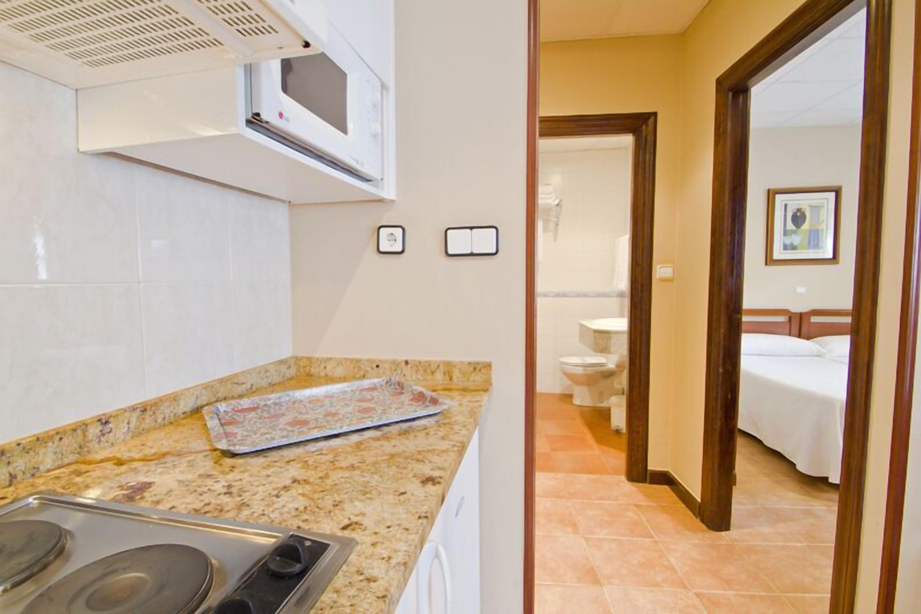 A kitchen with a microwave, stove, and a tray on the counter. There is a bathroom visible through an open door.