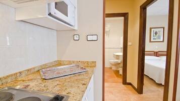 A kitchen with a microwave, stove, and a tray on the counter. There is a bathroom visible through an open door.
