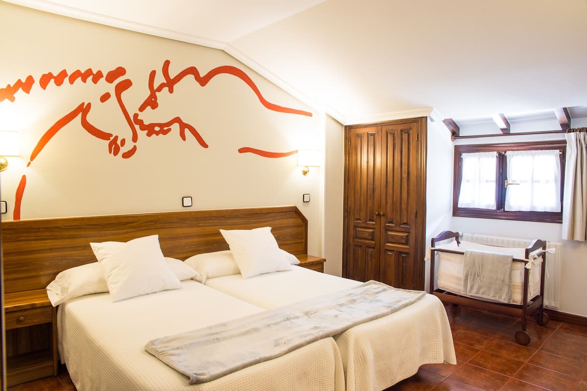 Une chambre d’hôtel avec un grand lit, une armoire en bois, une fenêtre avec des rideaux et un mur orné d’un motif abstrait rouge.