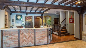 Un área de recepción con mostrador de ladrillo, vigas de madera, un reloj, obras de arte enmarcadas y una escalera que sube a otro piso.